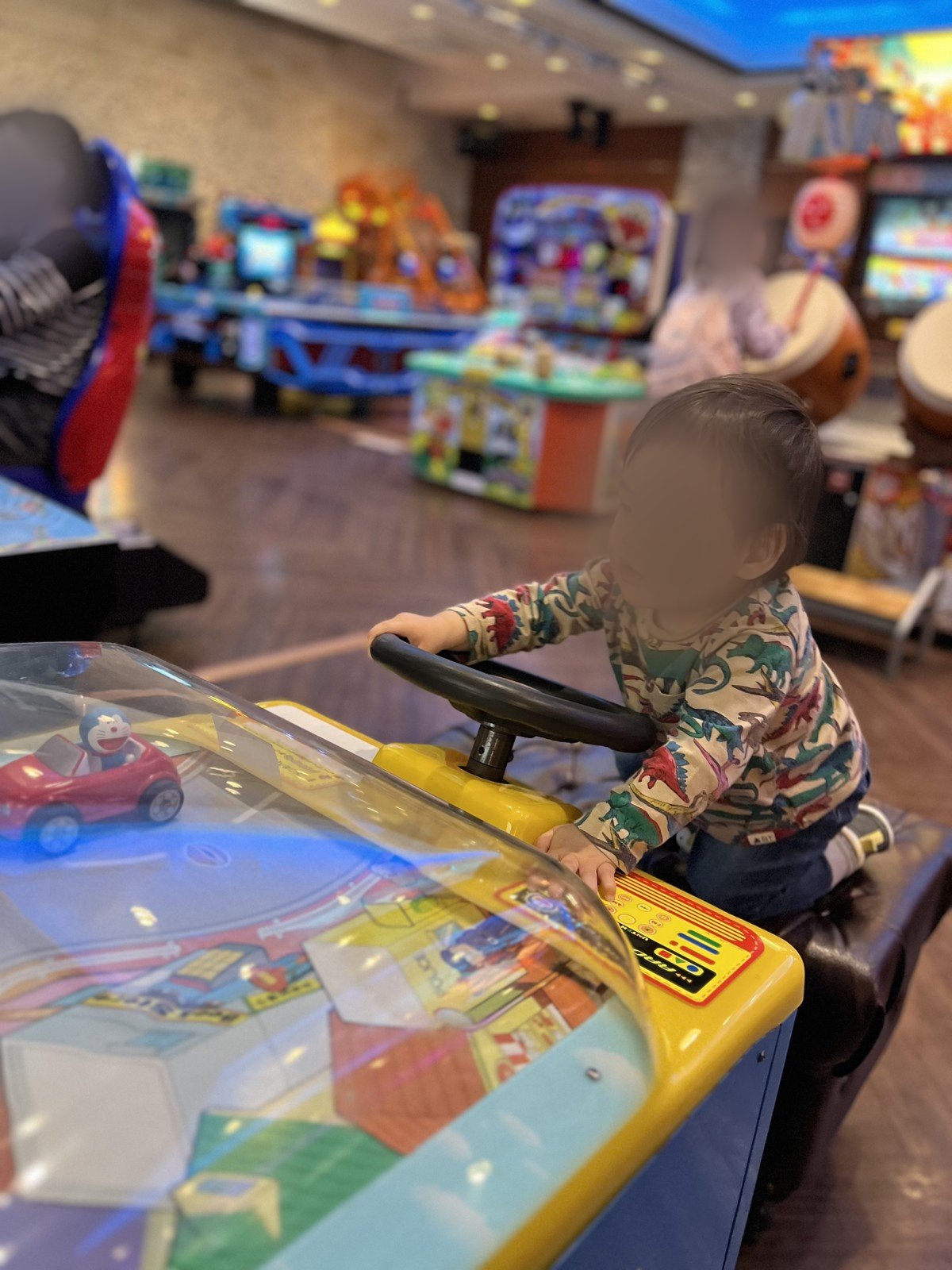 ドラえもんの運転ゲームで遊ぶ次男。奥には太鼓のゲームも