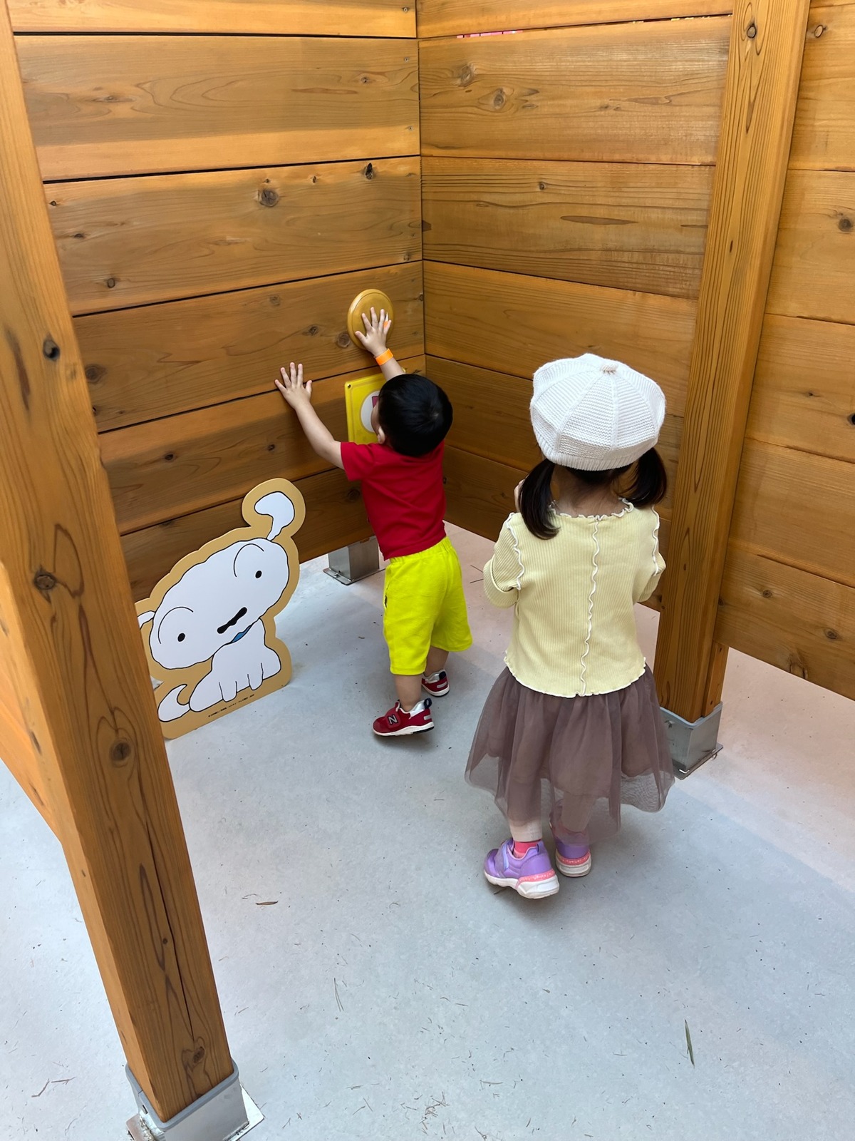 木の壁に取りつけられたボタンを押す子どもたち