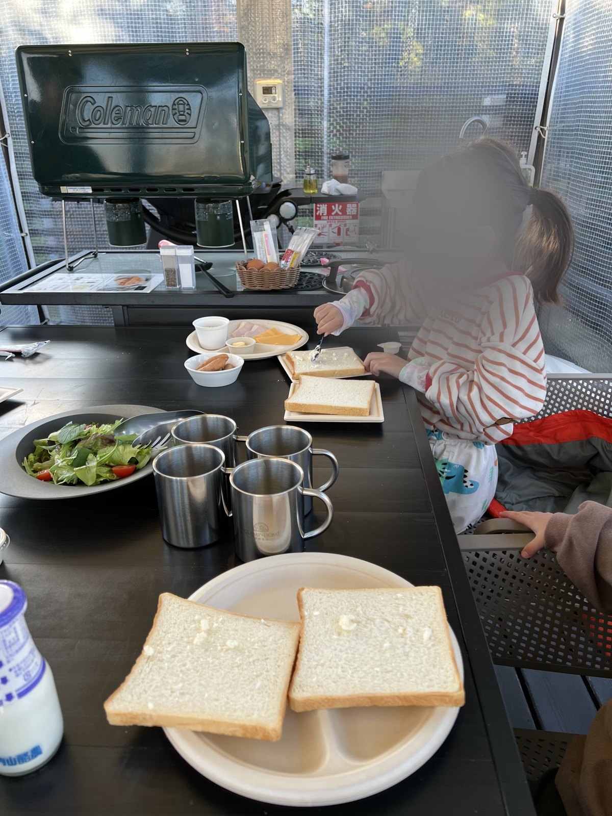 食パンにバターをぬる長女。テーブルにはサラダやハム、チーズが並ぶ