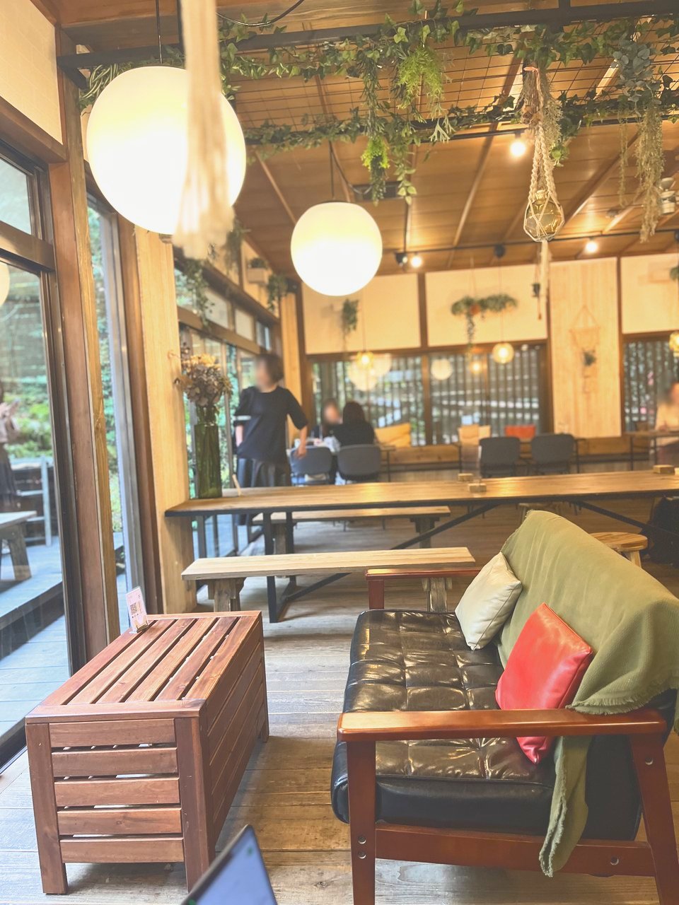 ペンダントライトとグリーンが下がる、木のテーブルが並ぶ店内