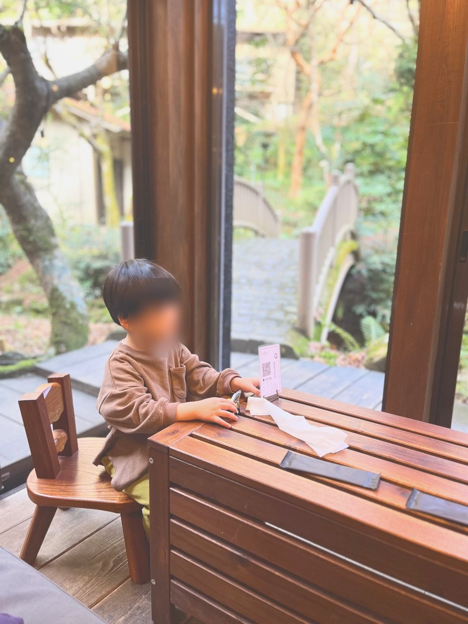 窓ぎわの木のテーブル席に座る子ども。窓の外に庭の橋が見える