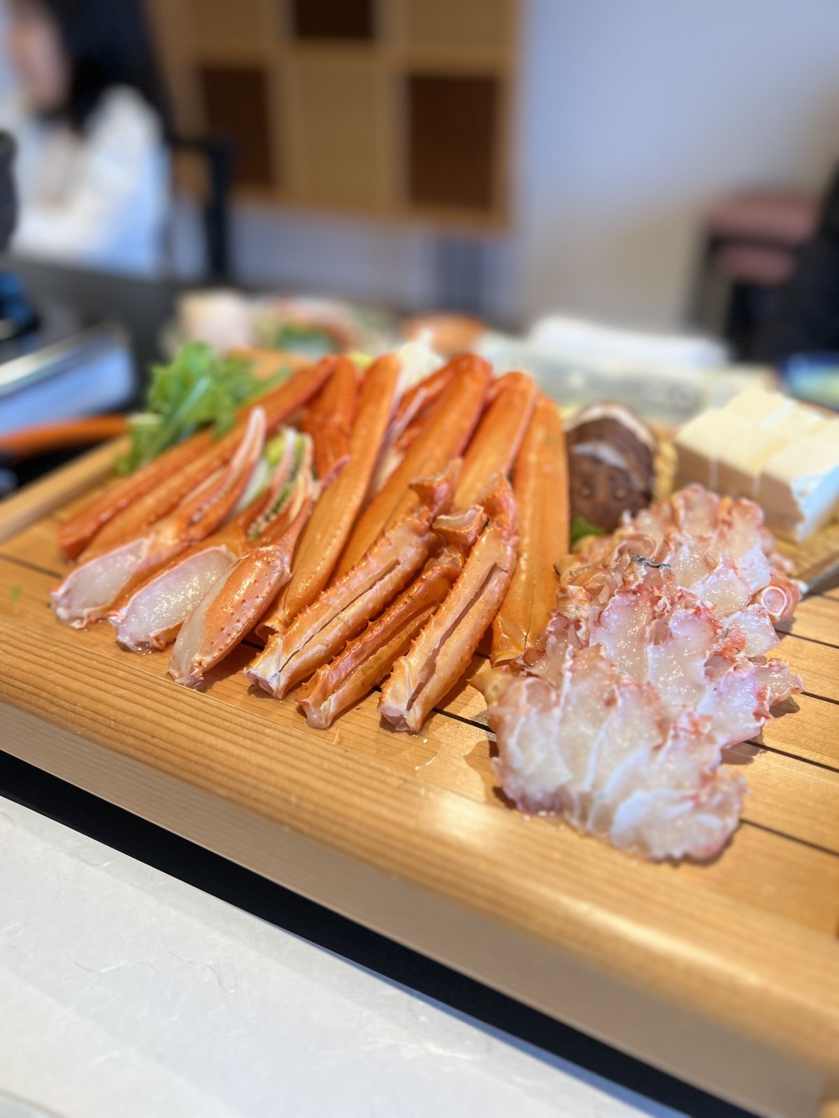 木の盆に盛られた、カニしゃぶ用のカニの脚と野菜・豆腐