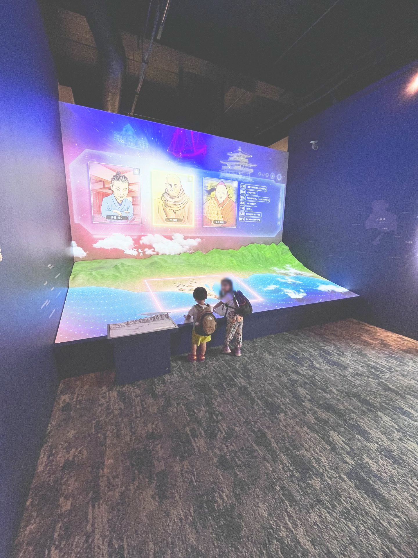 壁と展示台に映像が映る常設展示を見ている子どもたち