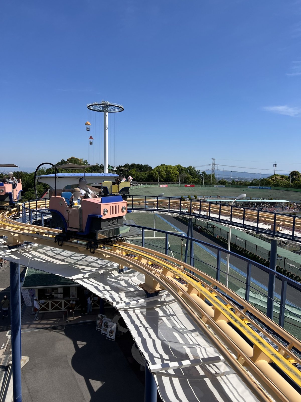 高いレールの上を走るピンクのスカイサイクルウォーカーと、奥に見えるサイクルパラシュートの塔
