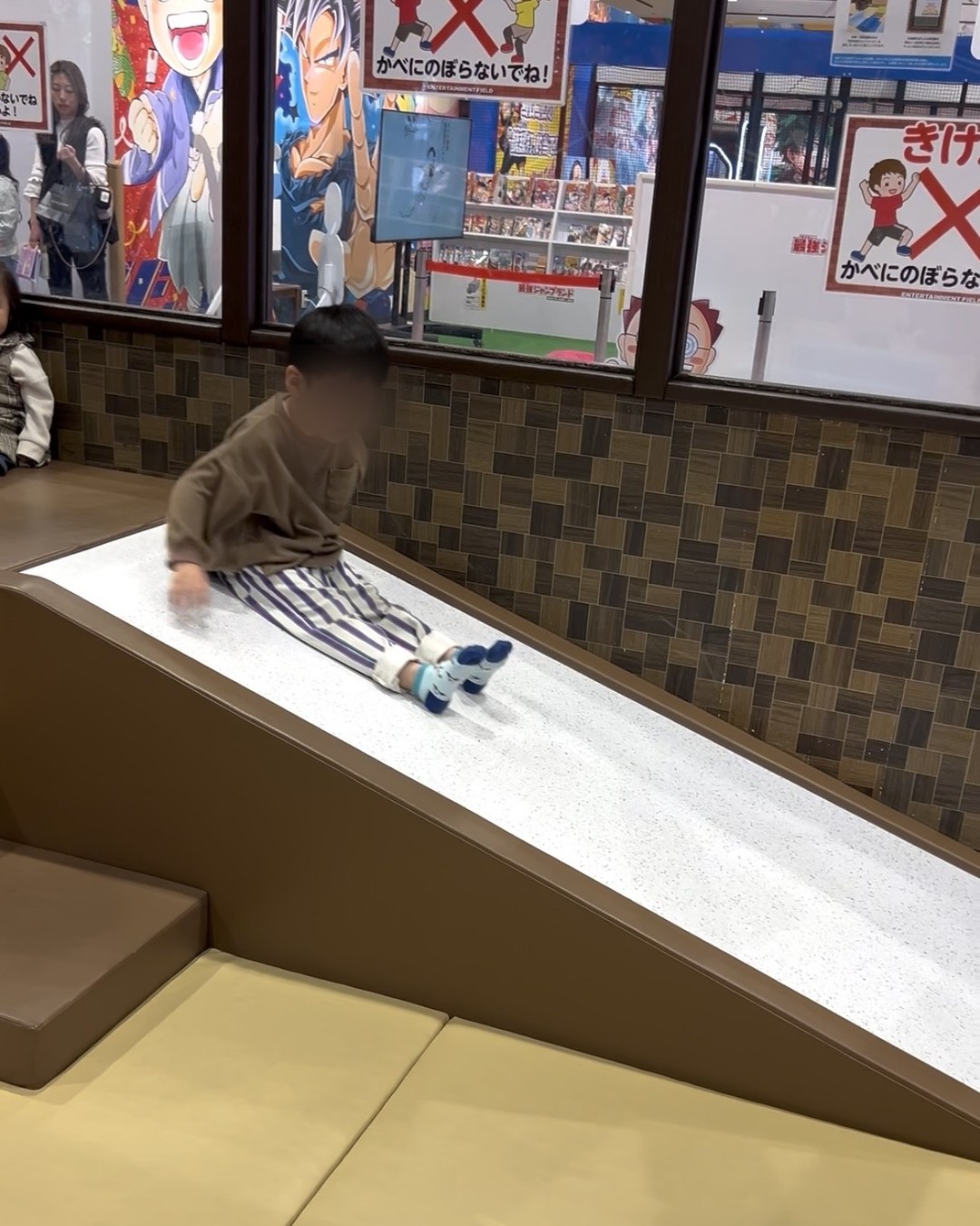 屋内キッズスペースの滑り台をすべる子ども