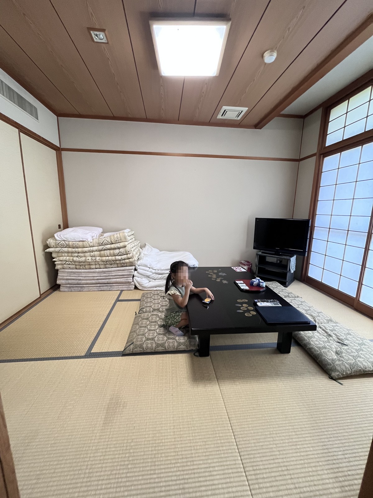 押入れの前に布団が積まれた和室。座卓とテレビがある
