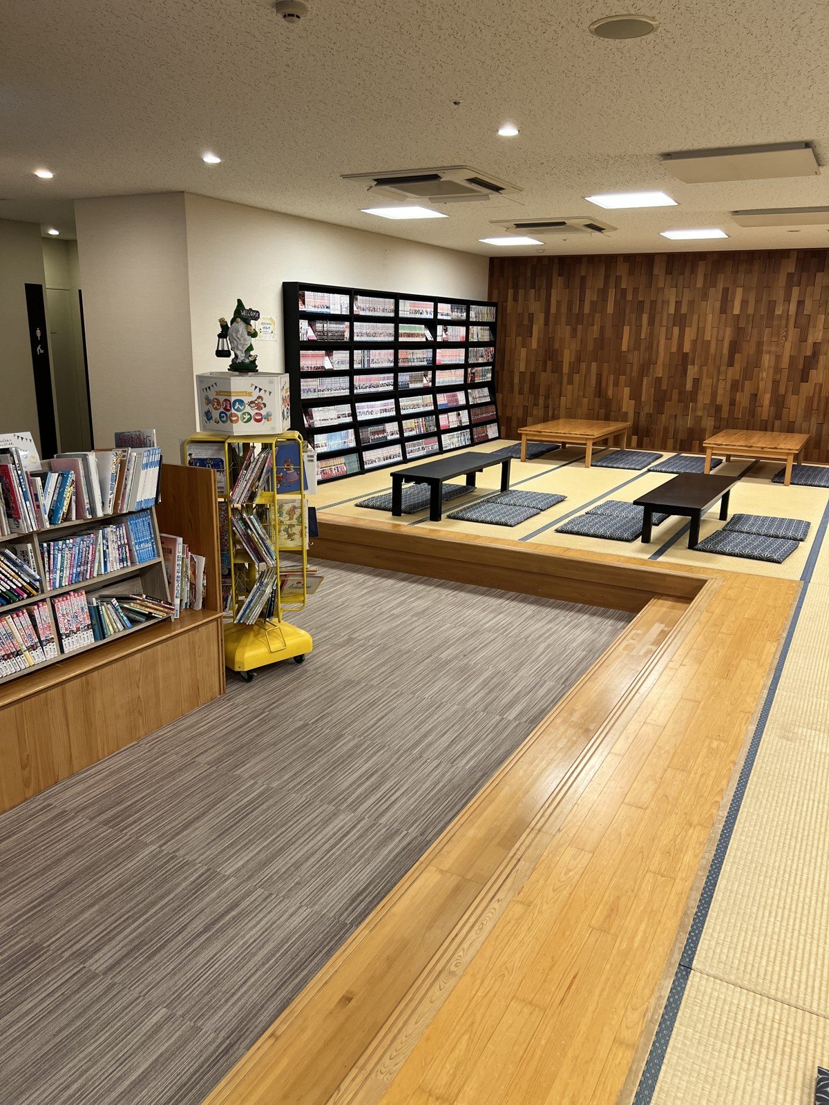 畳の小上がりと、壁一面の漫画の本棚、絵本の棚があるコーナー