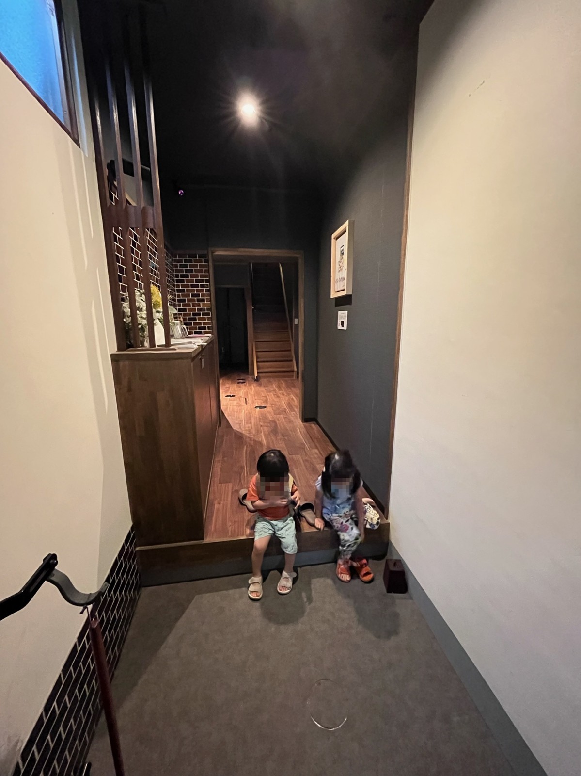 玄関の上がり框に腰かけて靴を履く子ども
