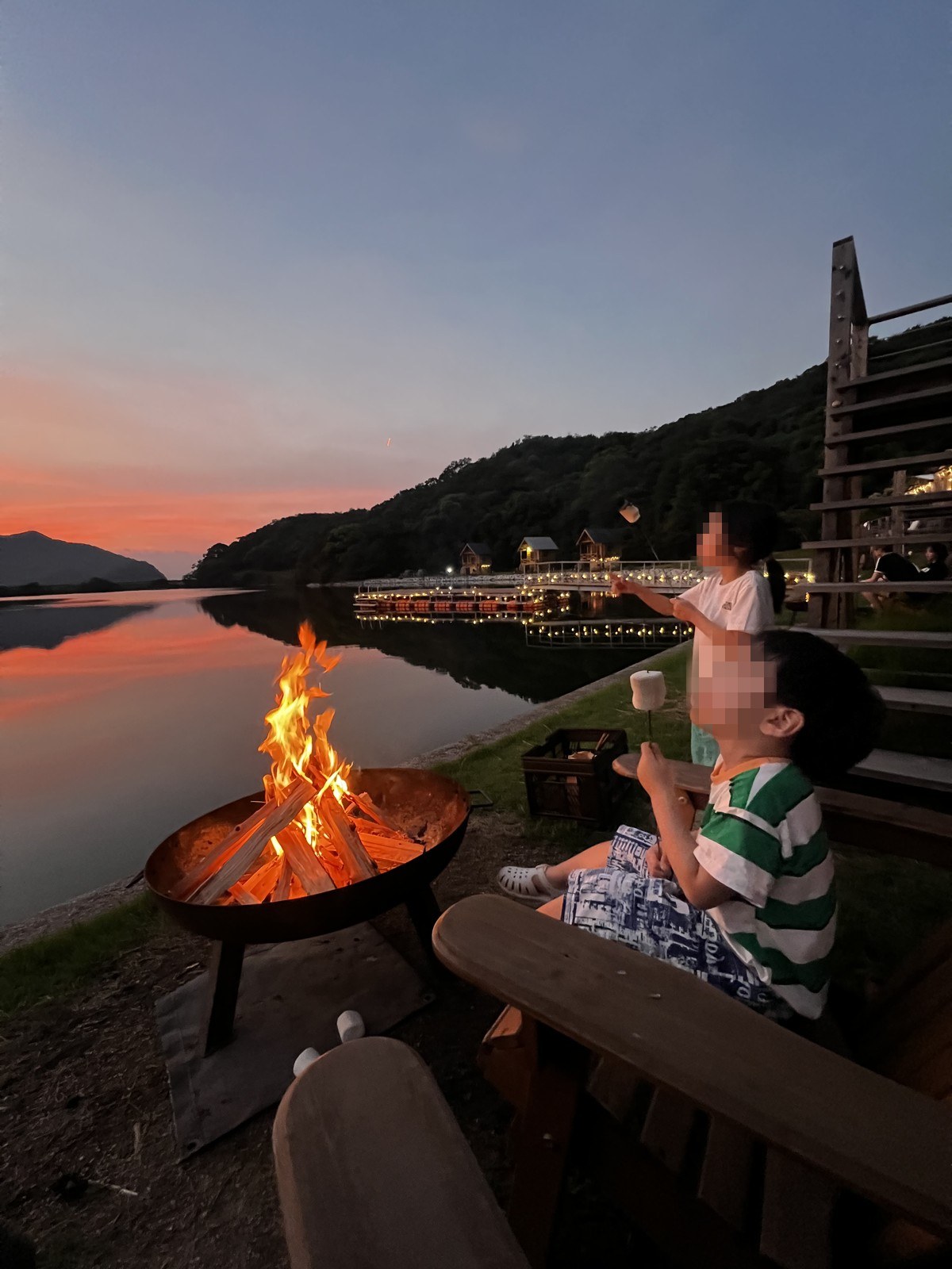 夕焼けの水辺で焚き火を囲む子どもたち