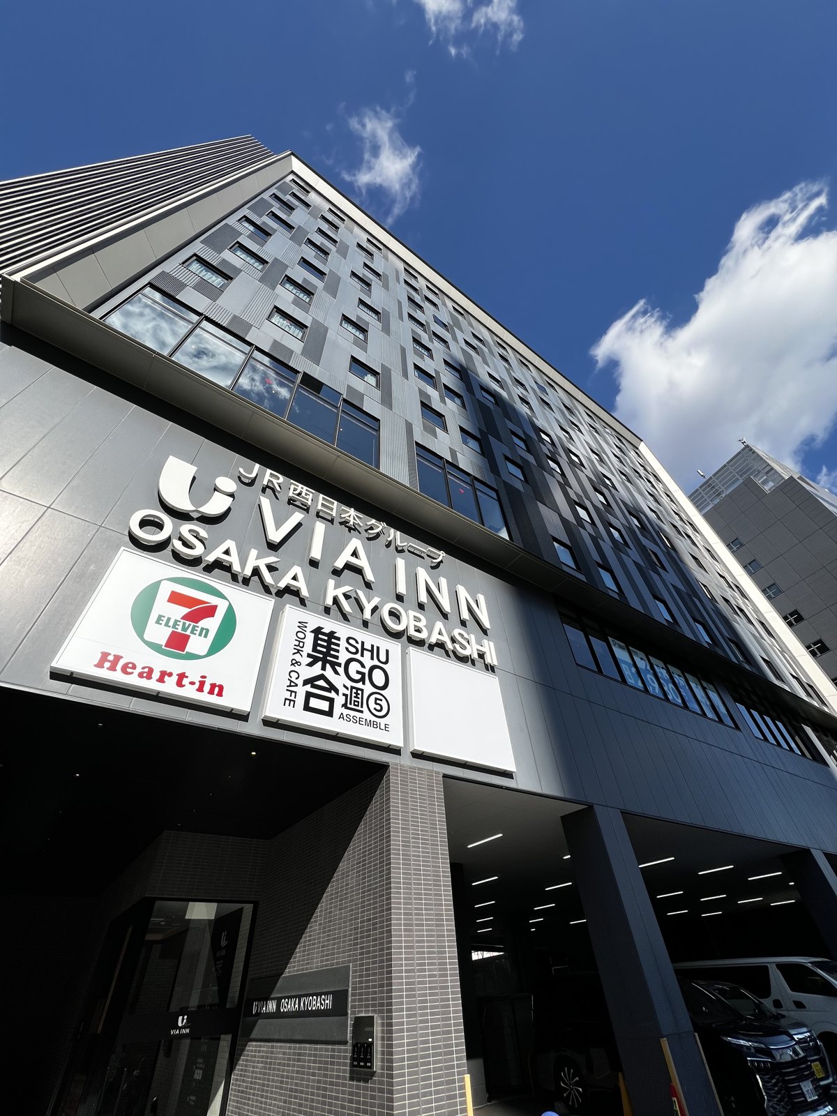 青空の下のホテル外観。1階にはコンビニも入っている