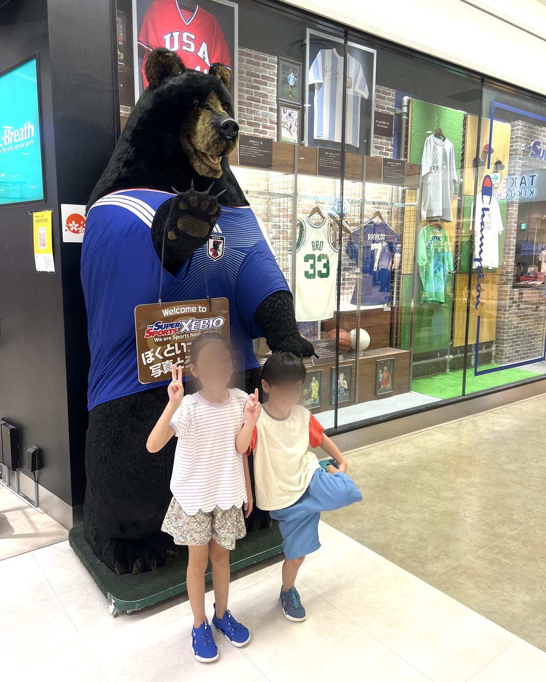 店頭のクマのマスコットと写真を撮る子どもたち