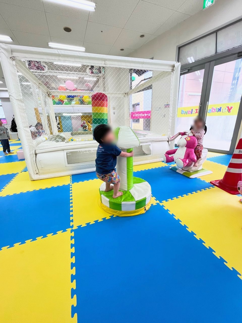 ボールプールの前で、乗り物の遊具に乗る子どもたち